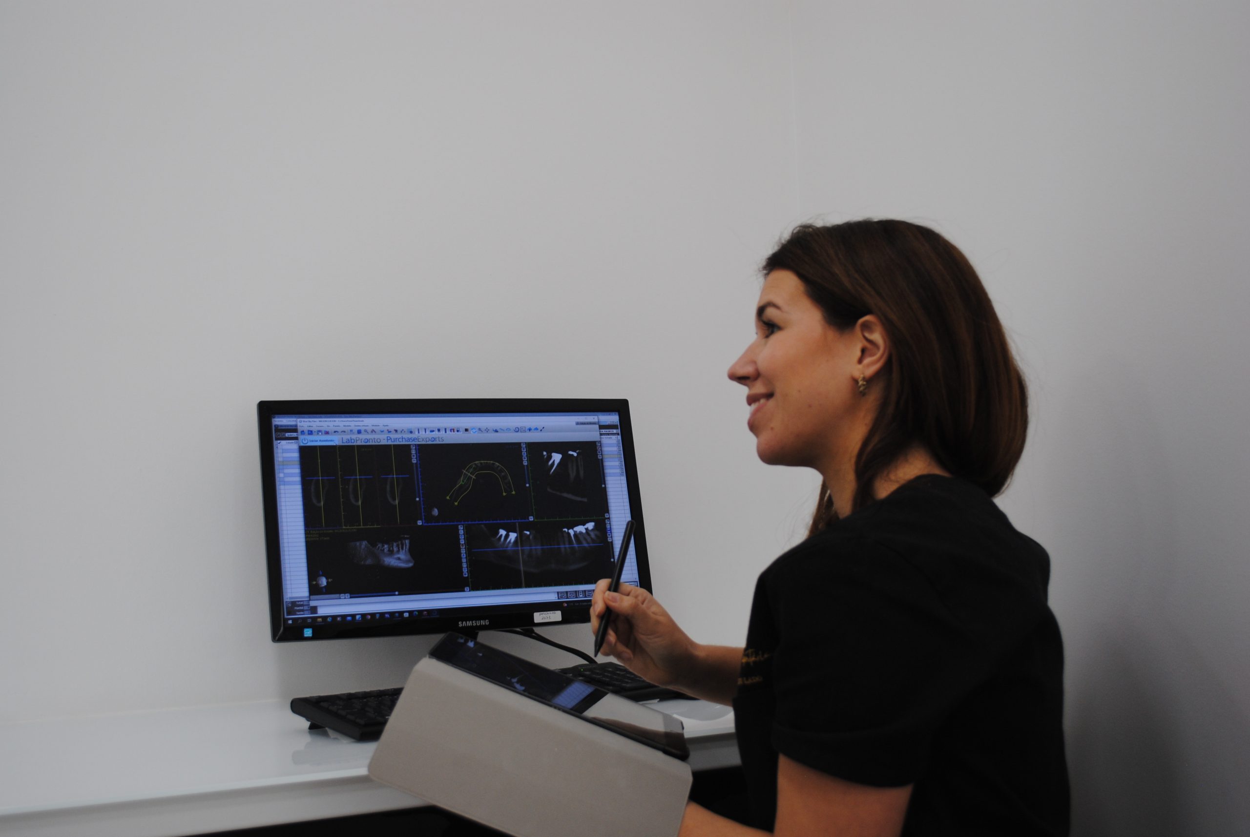 médica dentista a ver uma tac num computador enquanto segura num ipad e uma caneta
